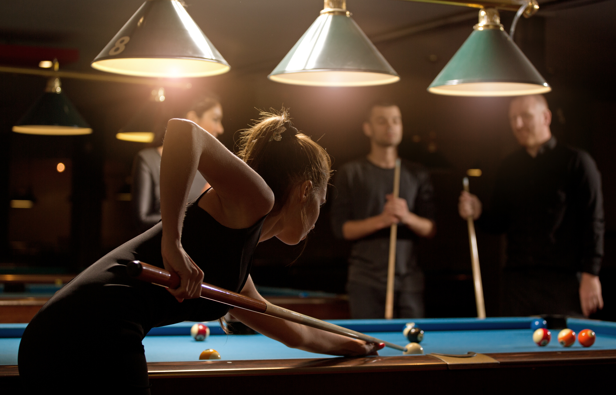 woman playing pool with group of friends