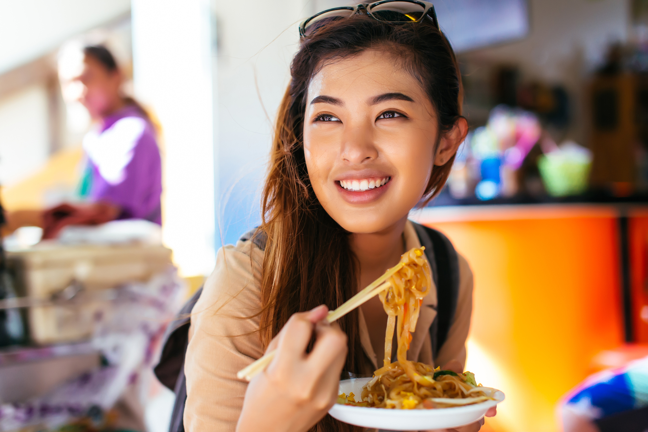 Young female tourist eating pad thai noodle at the shop