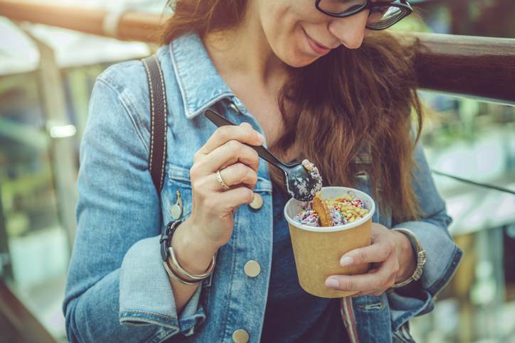 Young woman eating healthy rolled ice-cream or yogurt with fruits or berries, cookies, candy and mint