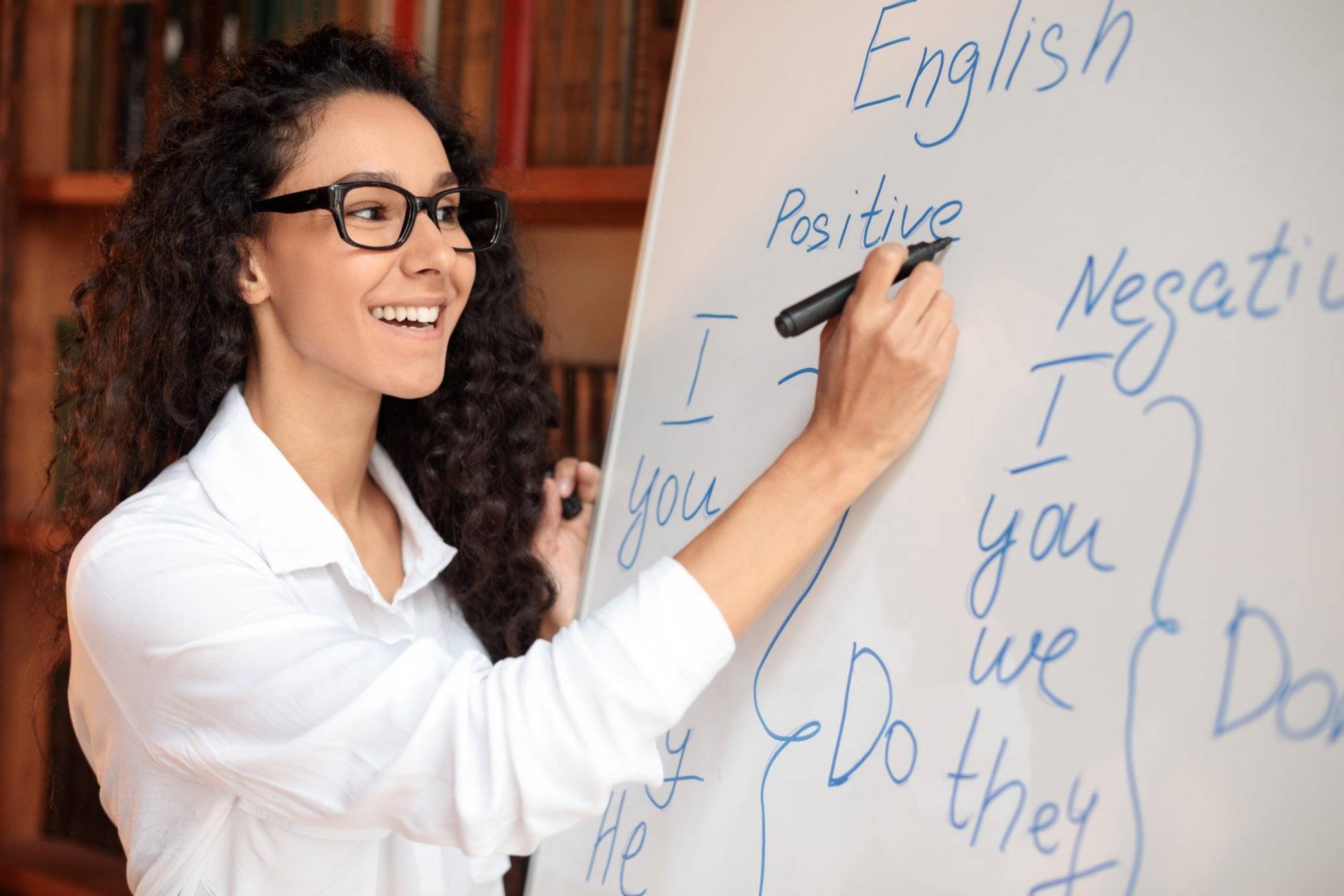 Smiling female teacher writing at whiteboard, explaining rules Smiling female teacher writing at whiteboard, explaining rules