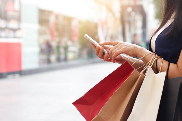 Woman using smartphone and holding shopping bag while standing on the mall background