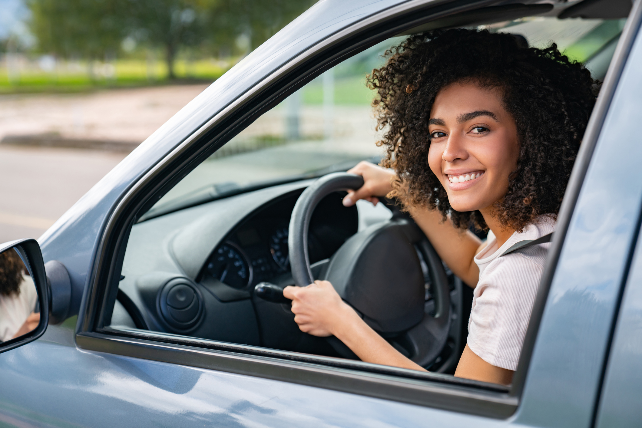 Portrait of a happy African American young woman driving her car and smiling at the camera through the window